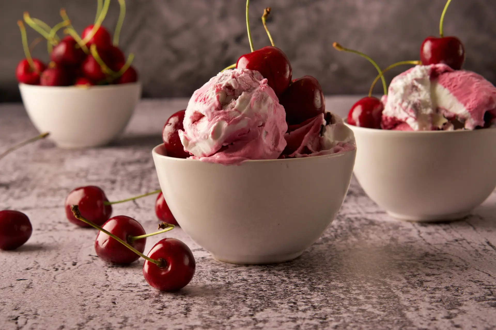 Pink ice cream scoop in white bowl decorated with cherries to enjoy on National Ice Cream Day.