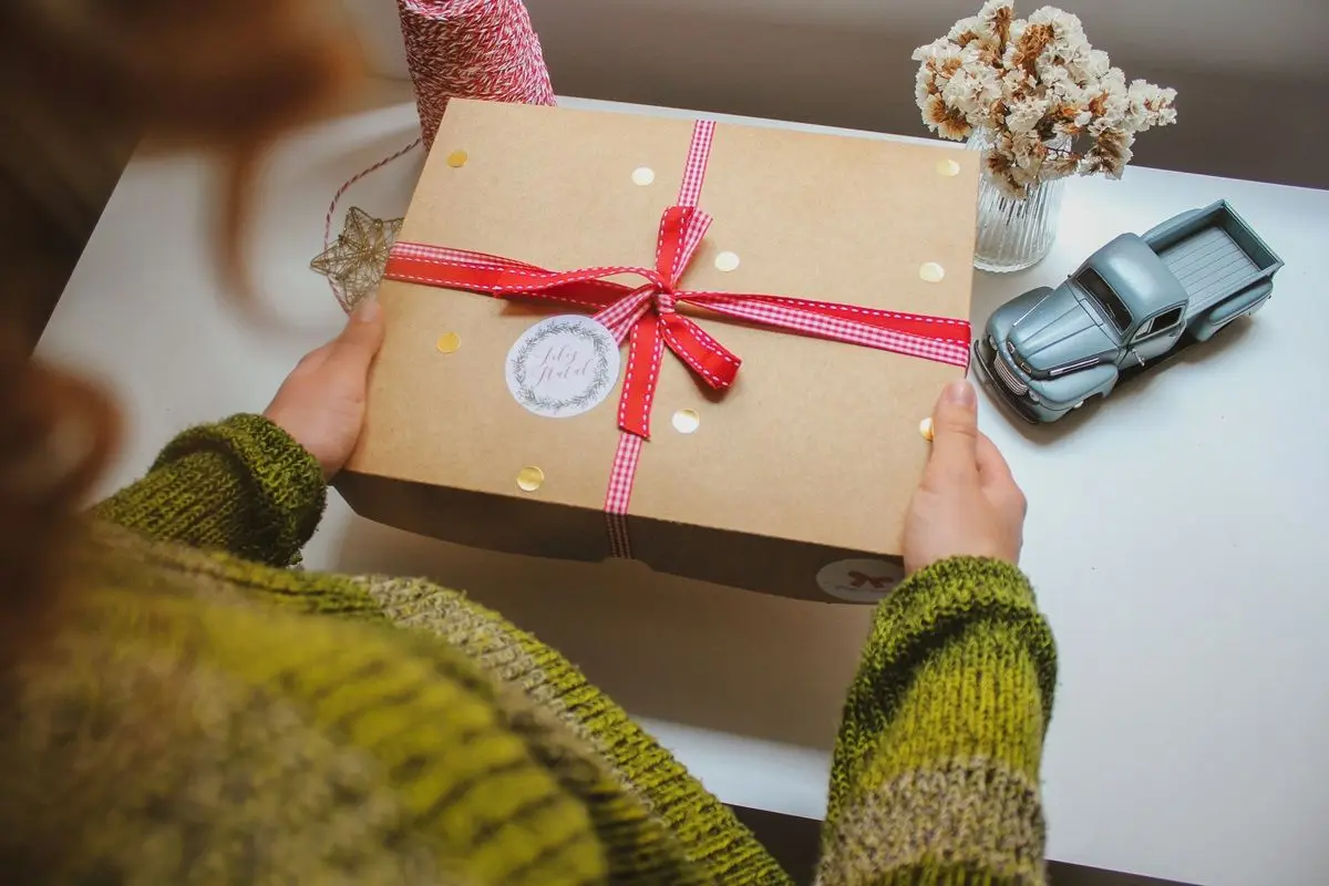 A person holding a gift box wrapped in gift paper and decorative rope.