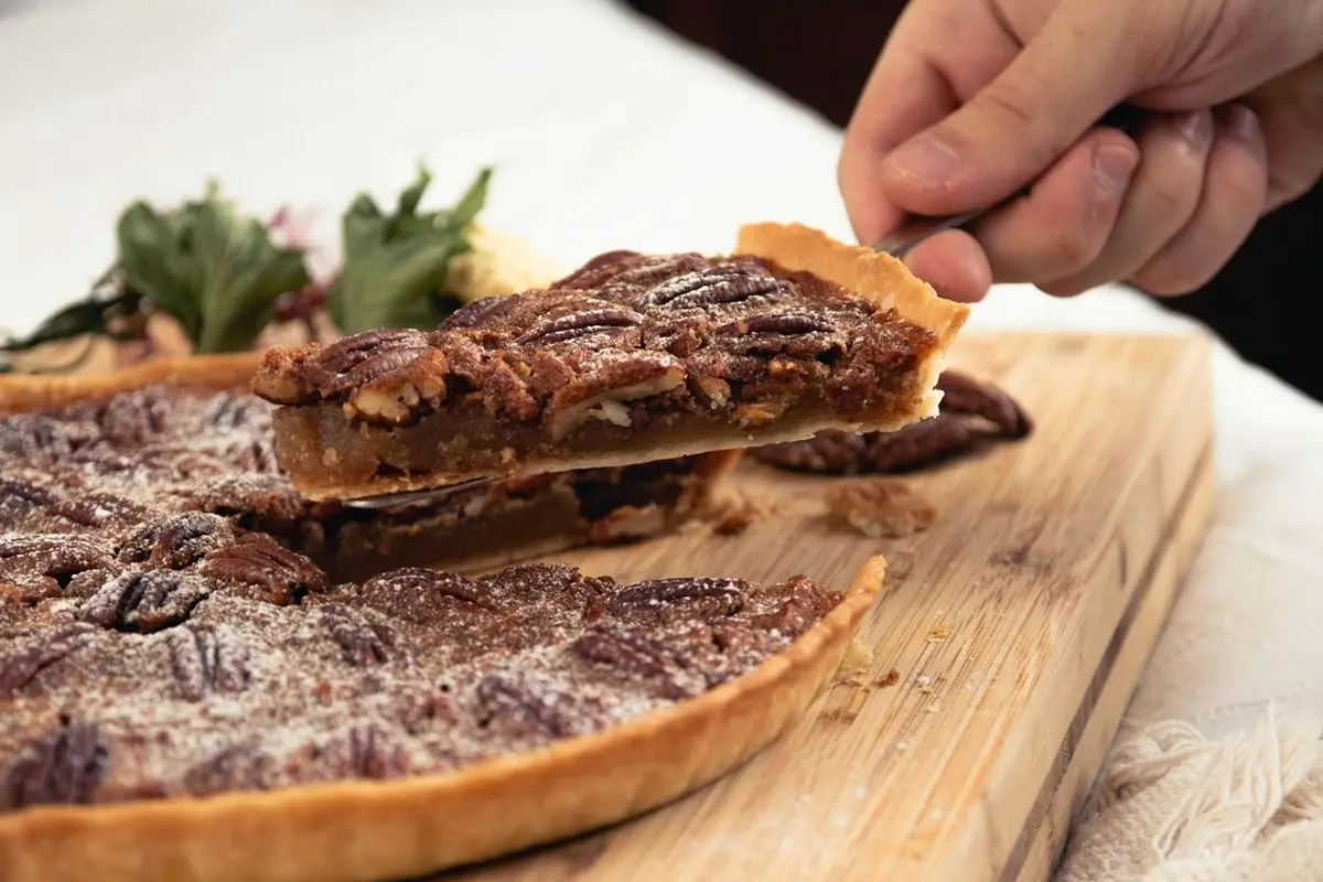 A hand holding a slice of mouthwatering pecan pie.