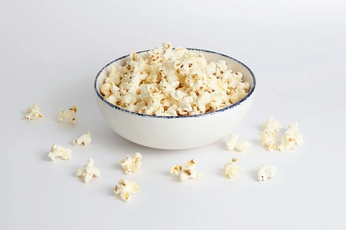 Popcorn in a white bowl placed on a white surface.