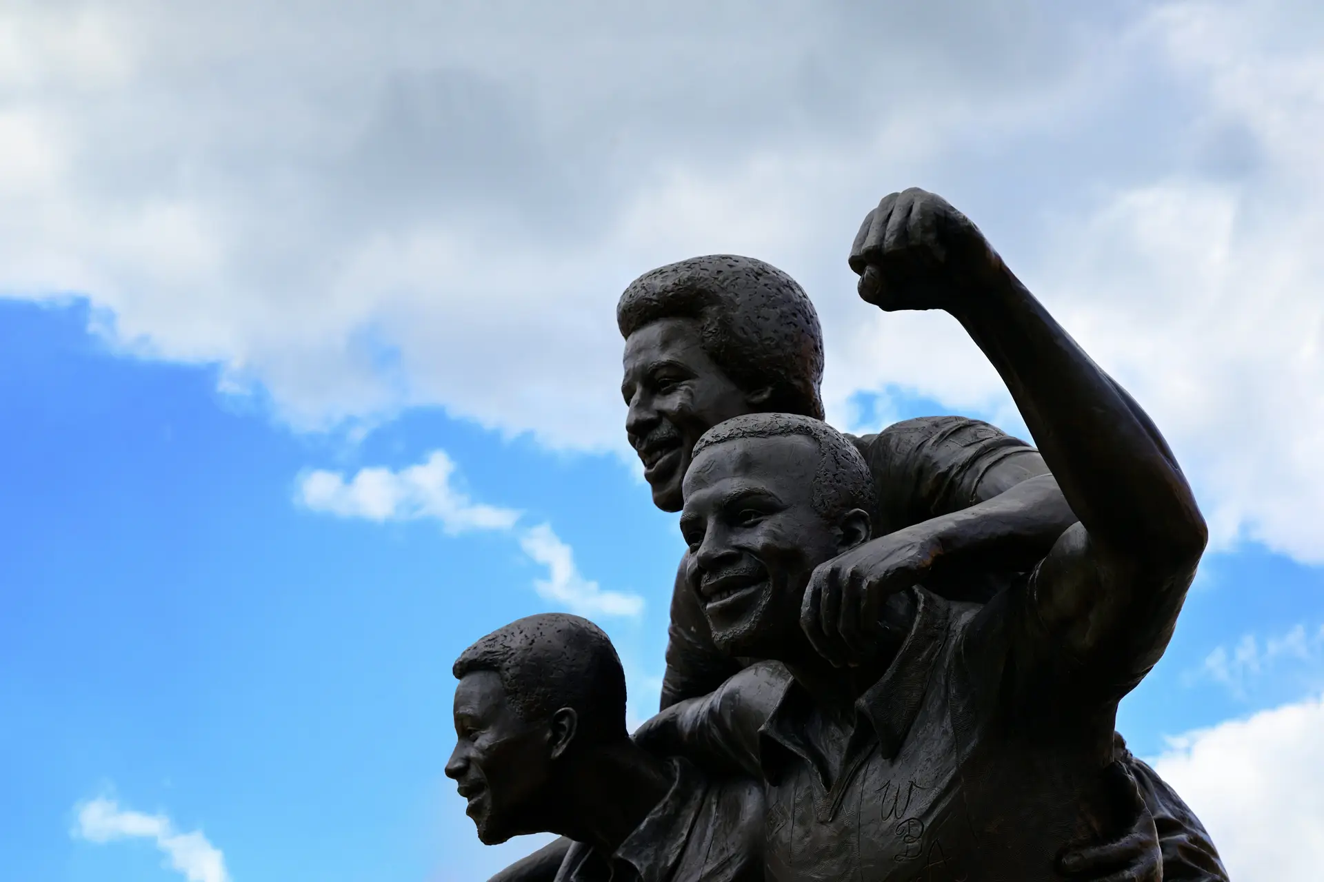 A statue of three men cheering, the blue open sky is in the background.