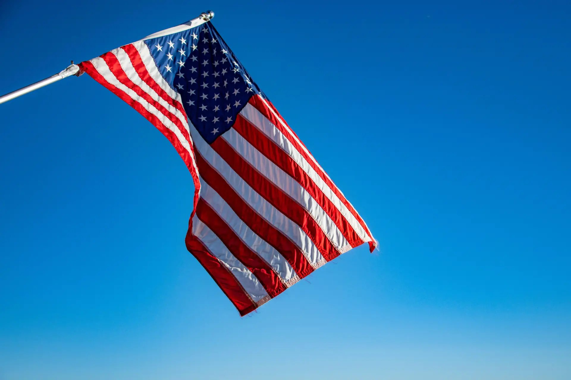 The flag of USA waving in the air. Behind it is the deep blue sky.