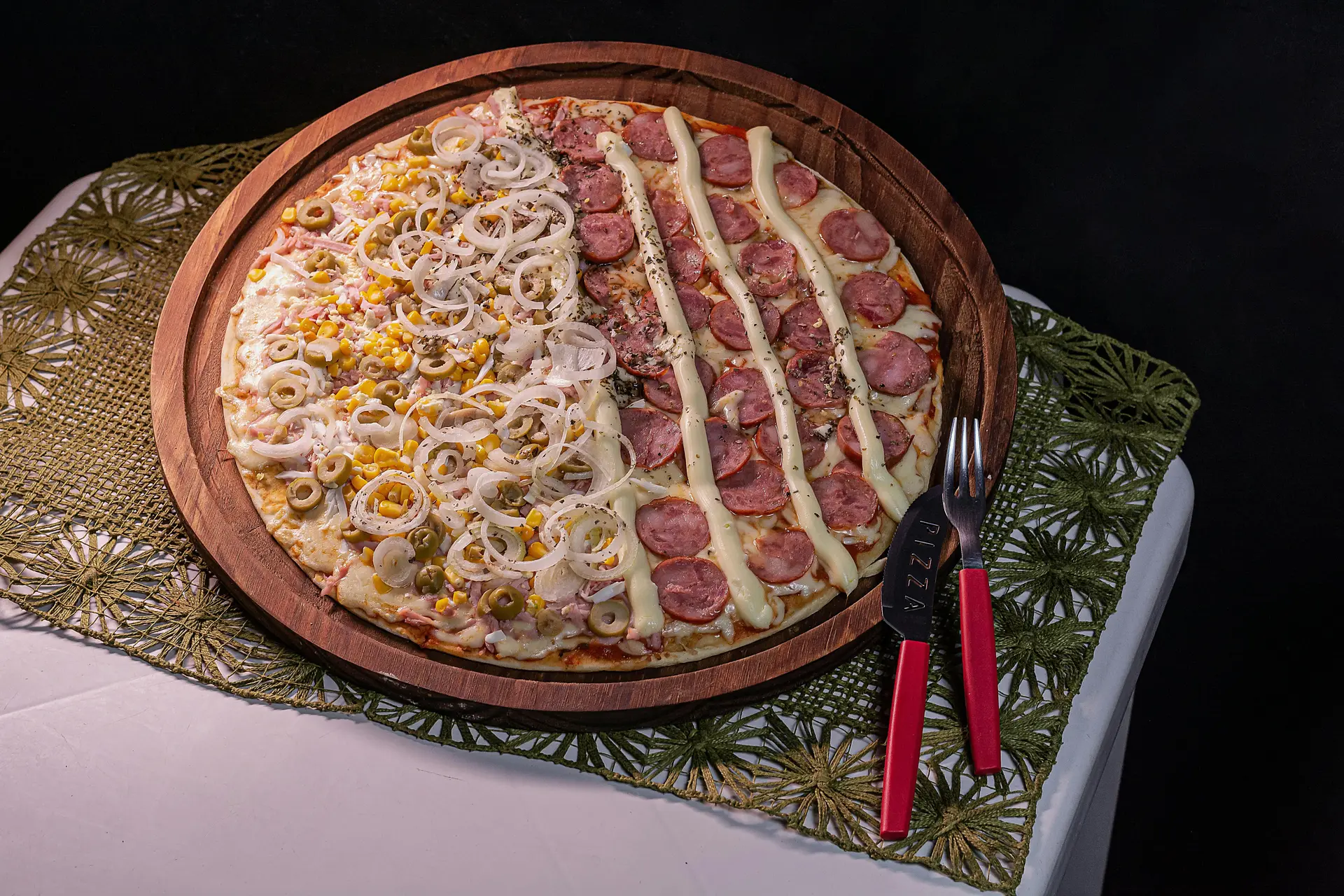 A sausage pizza with toppings such as sausage, onion rings is placed on a round platter along with a fork and knife.