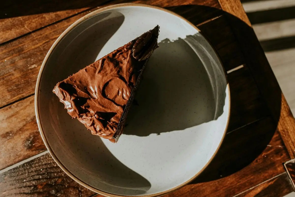 A slice of chocolate cake in a white plate on a wooden table.