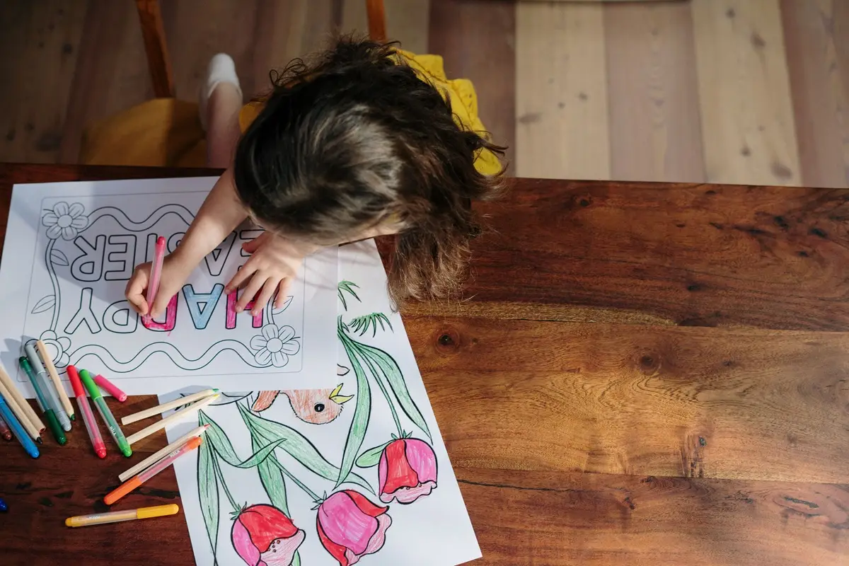 A child creatively colors Easter-themed artwork with vibrant markers on a wooden table.