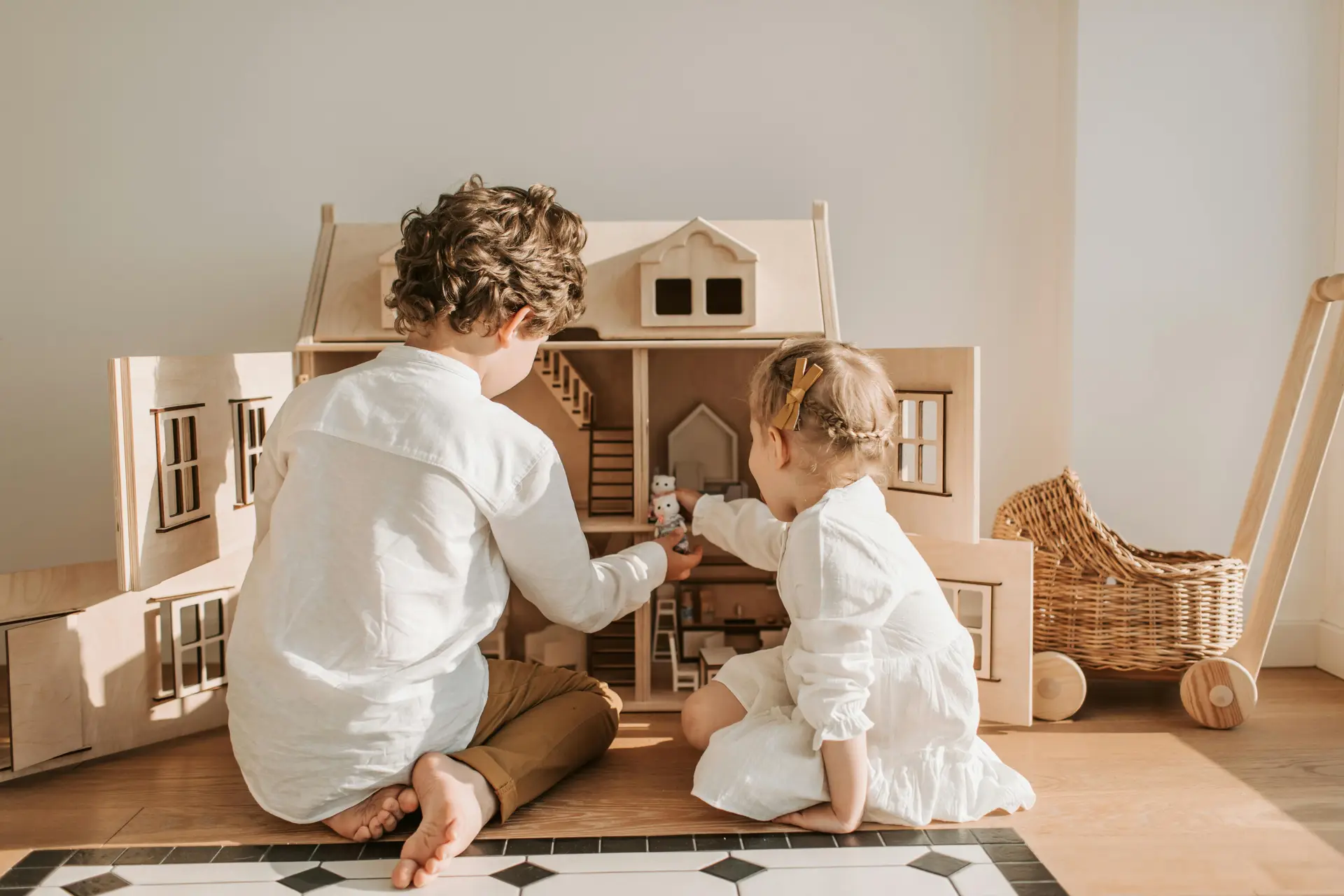 Big brother playing with his little sister with a doll house.