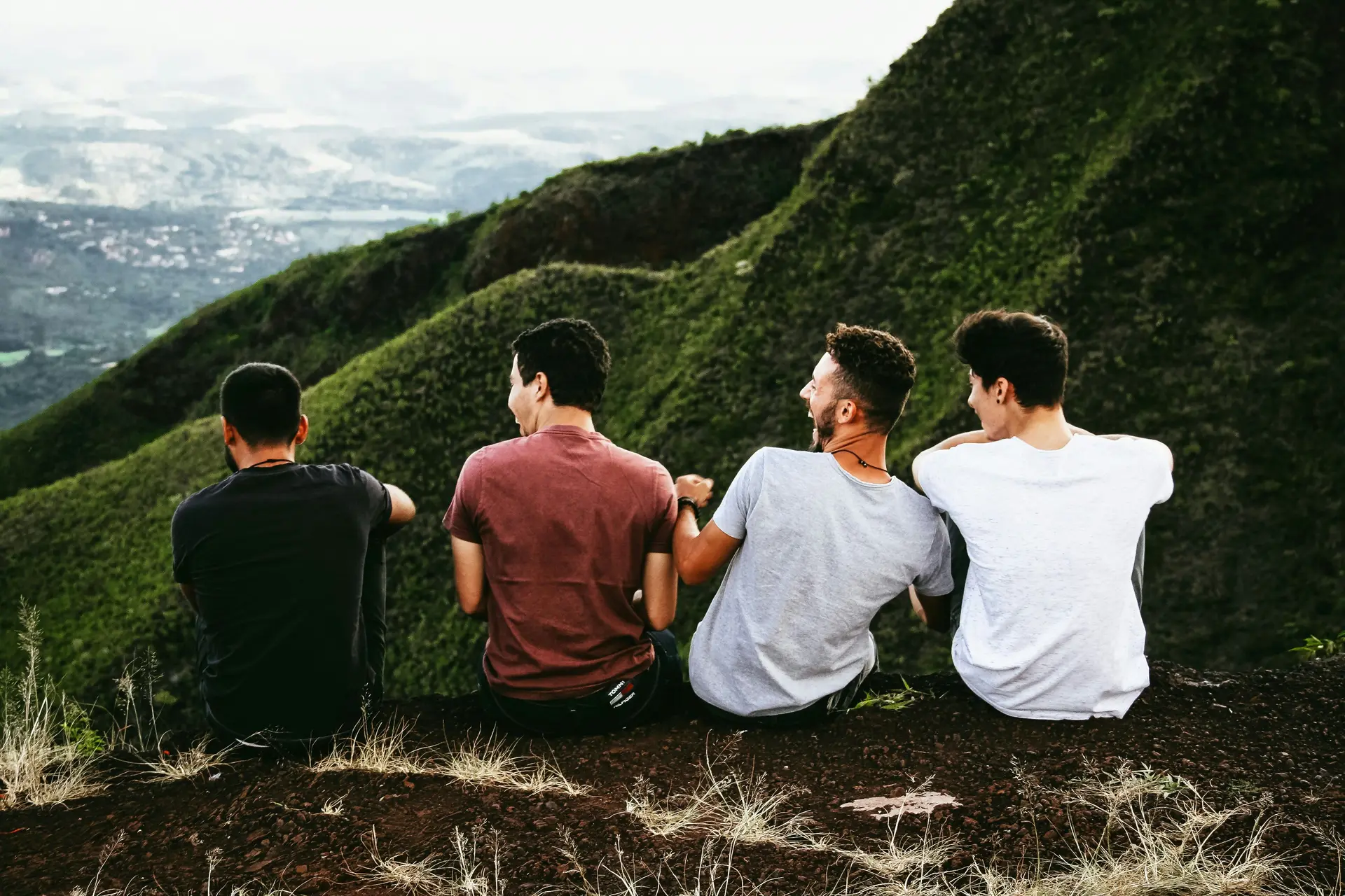 A row of four men sitting on mountain trail laughing.