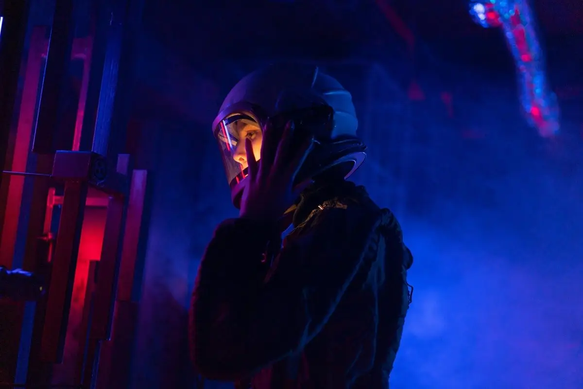 A woman in spacesuit holding her helmet. The atomosphere is dark and gloomy.