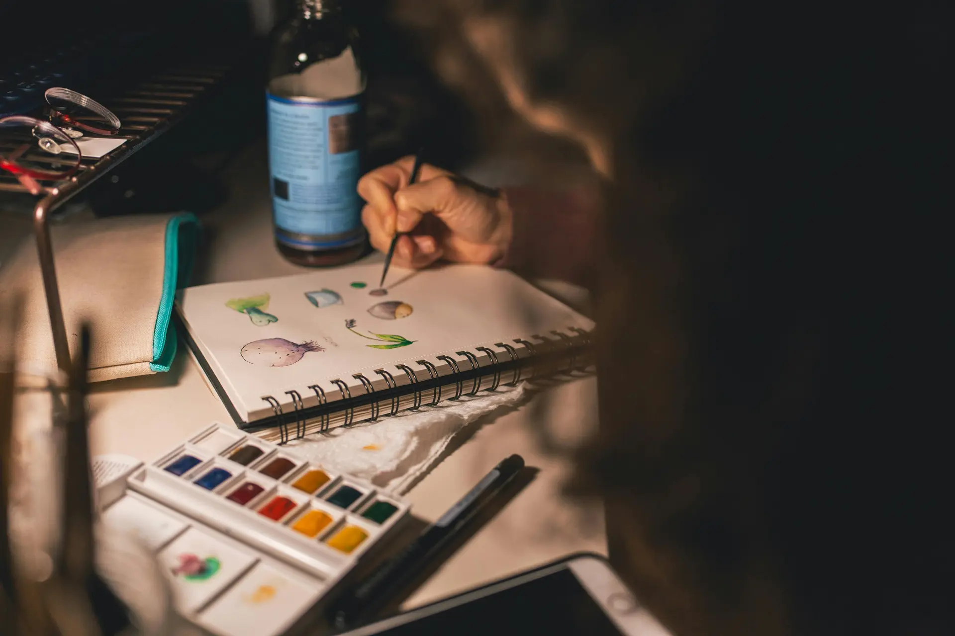 Person drawing illustrations in spiral notebook. There’s a swatch of color next to the notebook.
