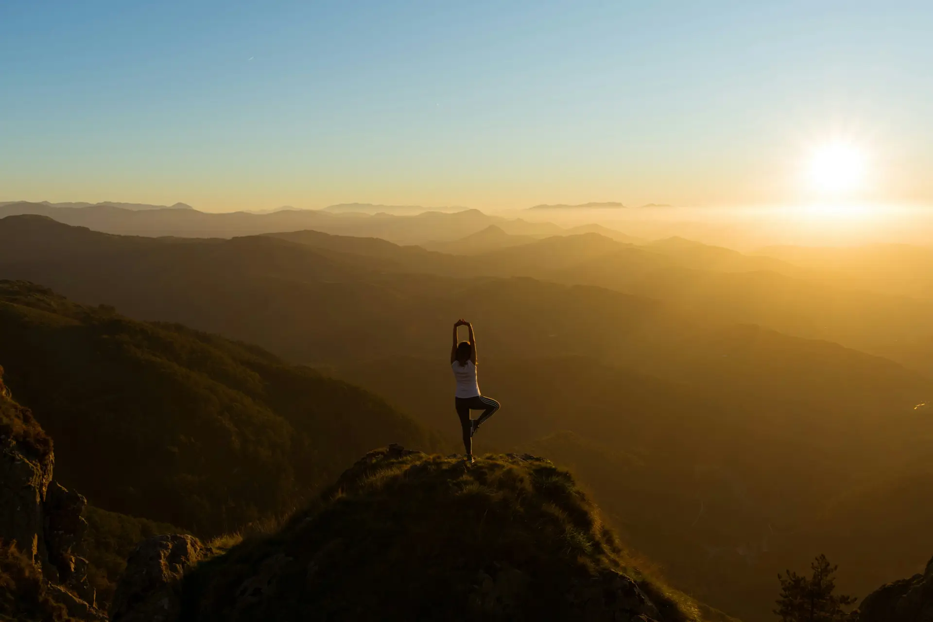 A woman practicing yoga on a hill top while the sun is setting.
