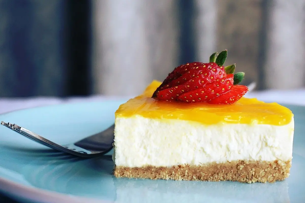 A fluffy creamy cake with a strawberry on it. The cake slice is placed on a plate along with a fork.
