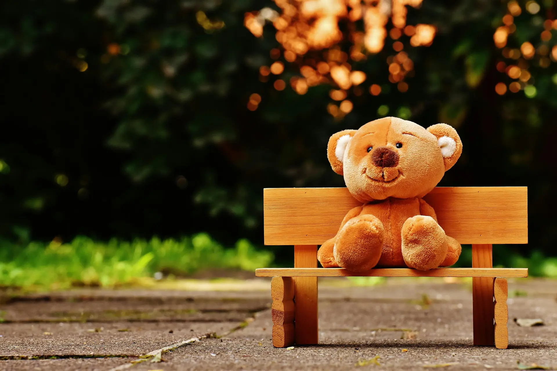A brown teddy bear sitting on a wooden bench outside.