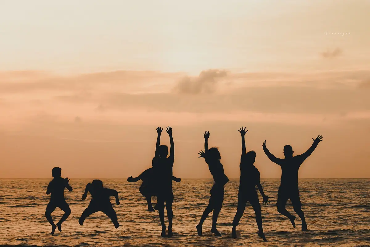 Silhouettes of people jumping joyfully at the beach during sunset with an orange sky.