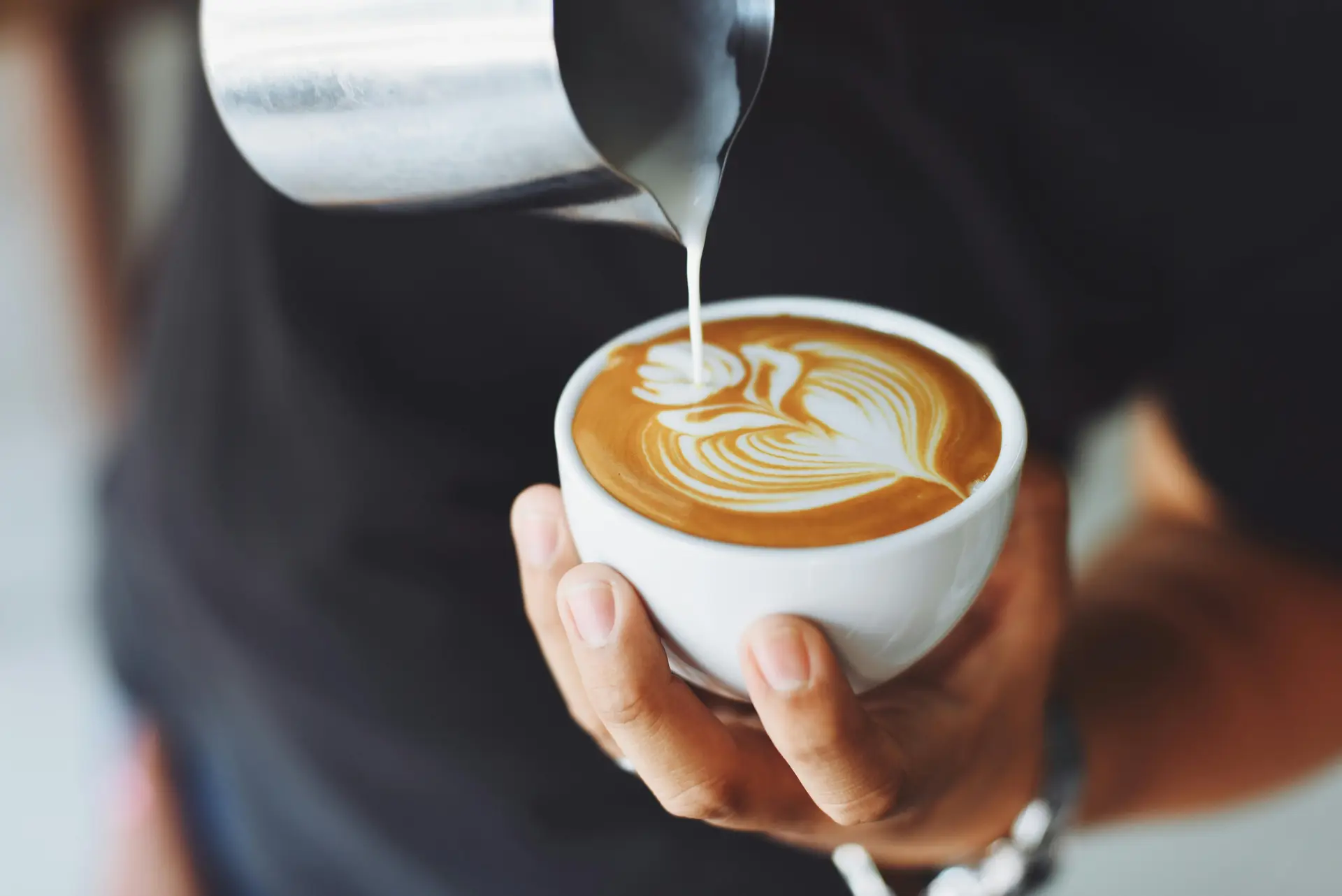 A barista making coffee art on a cup of coffee.