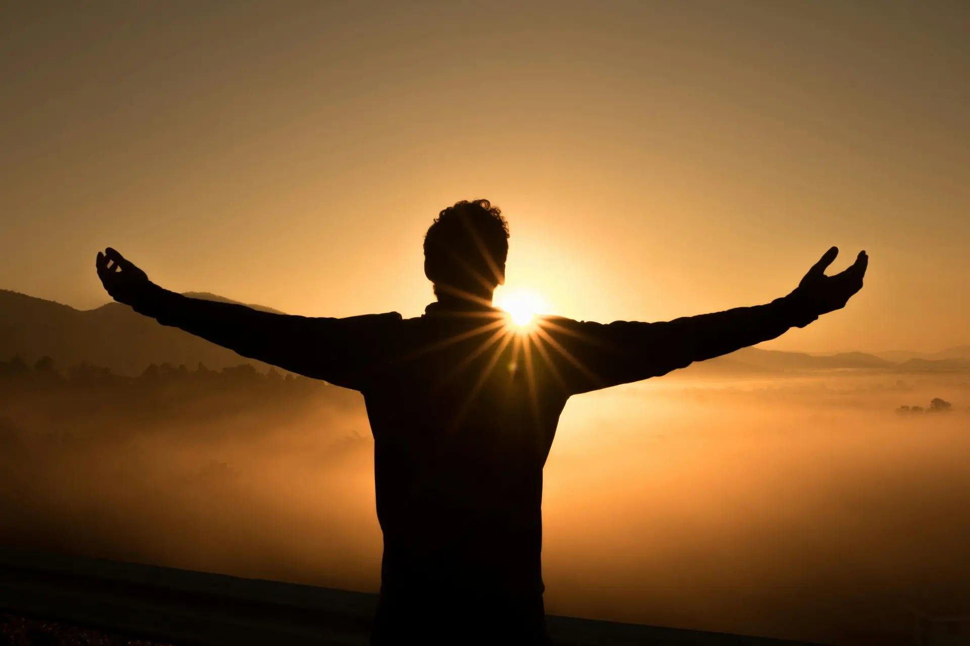 Silhouette of man on cliff during sunset.