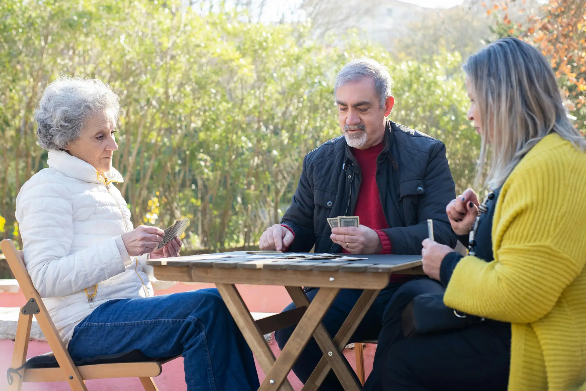 Elderly man and women playing cards in a park.