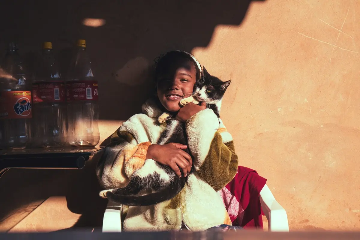 Young girl cuddling a girl while leaning on a wall.